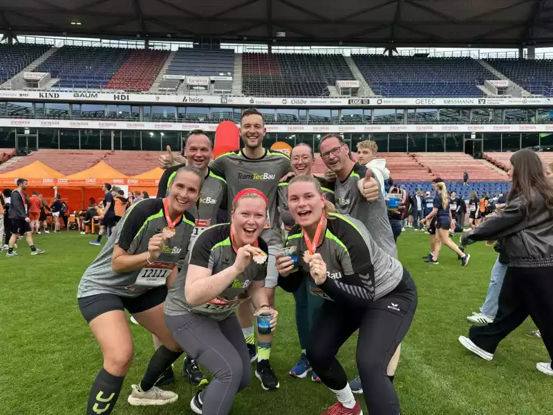 Läuferinnen und Läufer des TransTecBau-Teams beim B2Run 2025 am Maschsee in Hannover mit Zieleinlauf in der Heinz von Heiden Arena